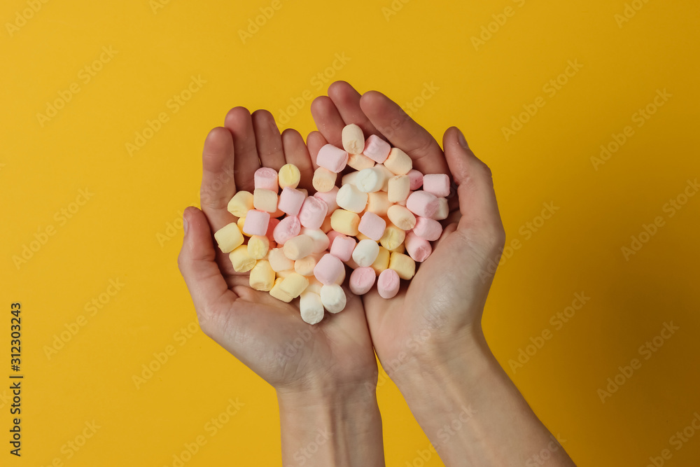 Lot of marshmallows in female hands on yellow background. Top view. Studio shot Lot of marshmallows in female hands on yellow background. Top view. Studio shot