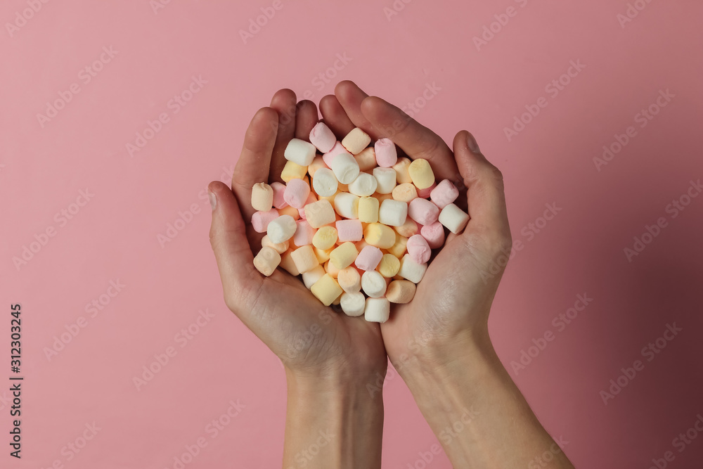 Lot of marshmallows in female hands on pink pastel background. Top view. Studio shot Lot of marshmallows in female hands on pink pastel background. Top view. Studio shot