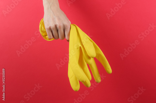 Female hands hold yellow gloves for cleaning on a red background. Home cleaning concept