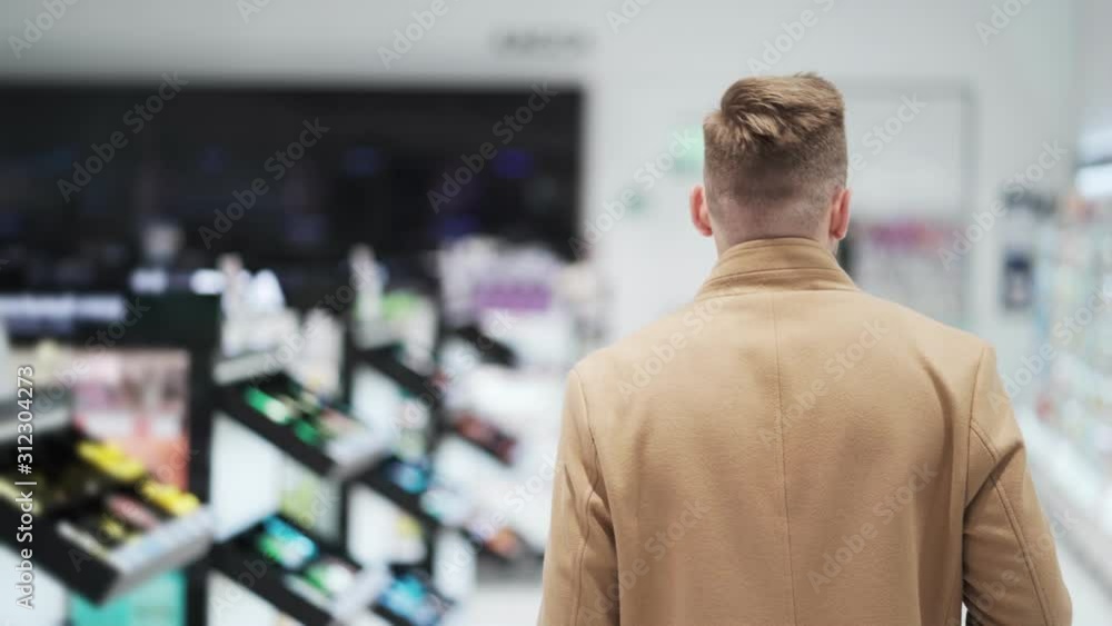 Backside view, young man in brown coat goes to shopping mall, steadicam shot Backside view, young man in brown coat goes to shopping mall, steadicam shot