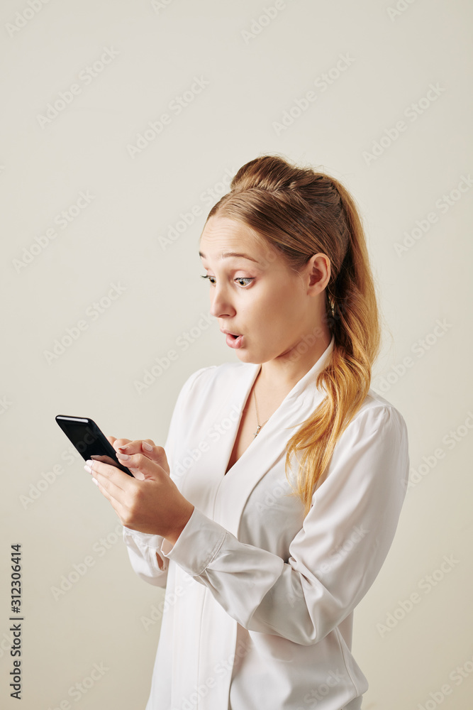 Shocked young woman reading text message with exciting news on smartphone Shocked young woman reading text message with exciting news on smartphone