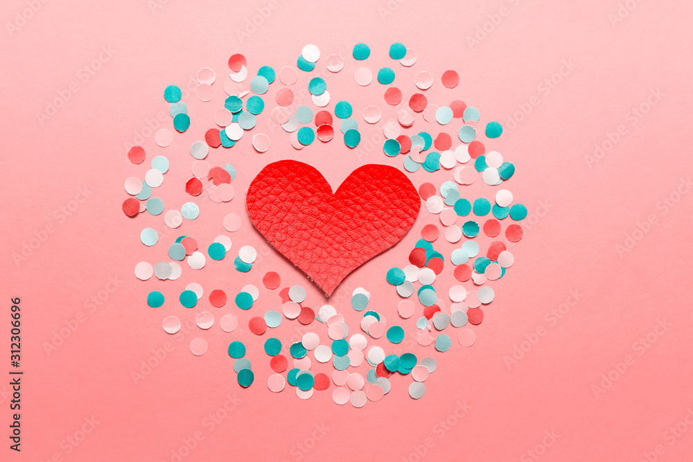 Red large fabric textile heart on pink background with blue white pink paper confetti.