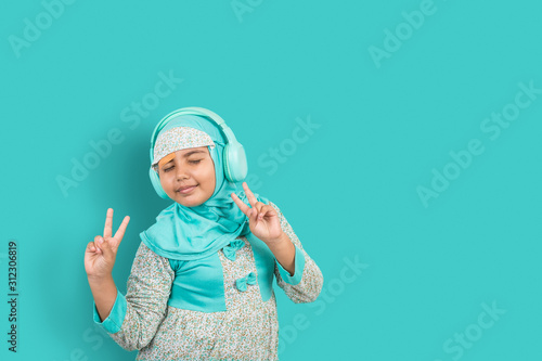 A young Asian girl wearing hijab listening to music on headphones dancing with her eyes closed