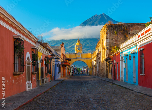 Cityscape of the main street and yellow Santa Catalina arch in the historic city center of Antigua at sunrise with the Agua volcano, Guatemala. photo