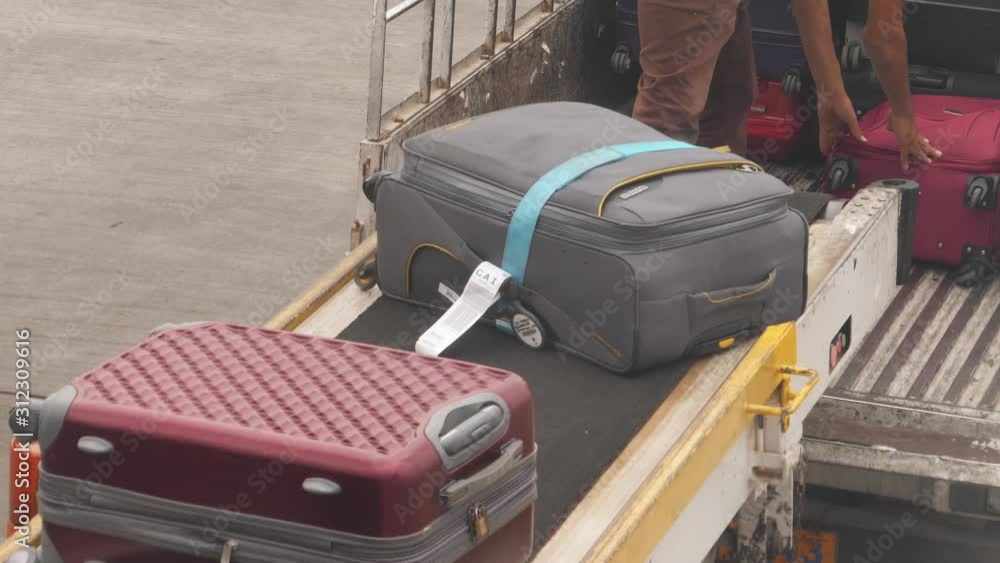 Baggage handlers unload an airplane with conveyor belt delivering suitcases to back of truck for transport to the terminal and waiting passengers. Suitcases moving on belt. Baggage handlers unload an airplane with conveyor belt delivering suitcases to back of truck for transport to the terminal and waiting passengers. Suitcases moving on belt.