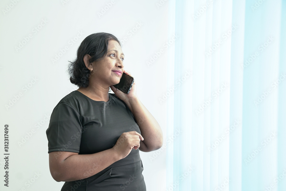 Smart and beautiful Indian corporate woman talking on her phone next to the office windows. Smart and beautiful Indian corporate woman talking on her phone next to the office windows.