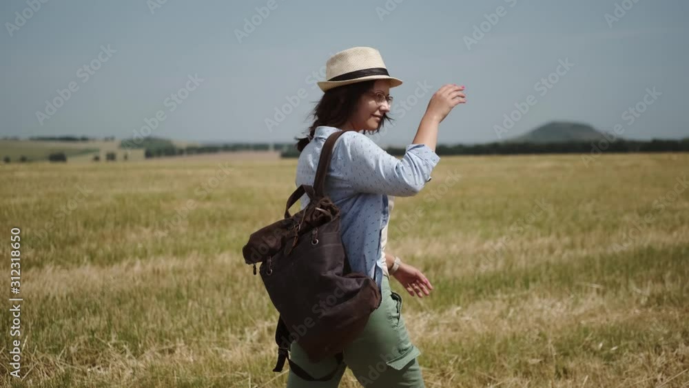 young woman traveler is walking with a backpack across the field young woman traveler is walking with a backpack across the field