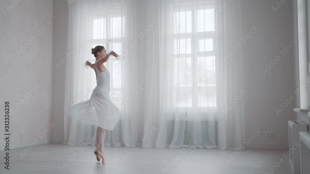 ballet dancer is spinning on tiptoe in a snow-white dress in a bright studio on the background of large windows ballet dancer is spinning on tiptoe in a snow-white dress in a bright studio on the background of large windows