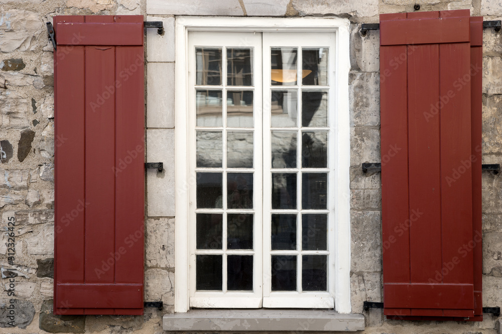 The facade of an old stone house with window and brown shutters The facade of an old stone house with window and brown shutters