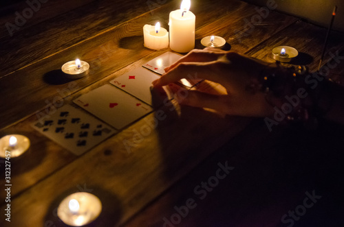 Hands of a fortune teller and cards on the table, around lit candles in the dark on a wooden table. concept of divination, magic