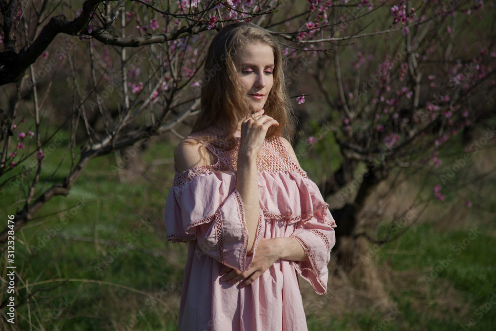 Beautiful blonde woman in pink dress in flowering garden in spring Beautiful blonde woman in pink dress in flowering garden in spring