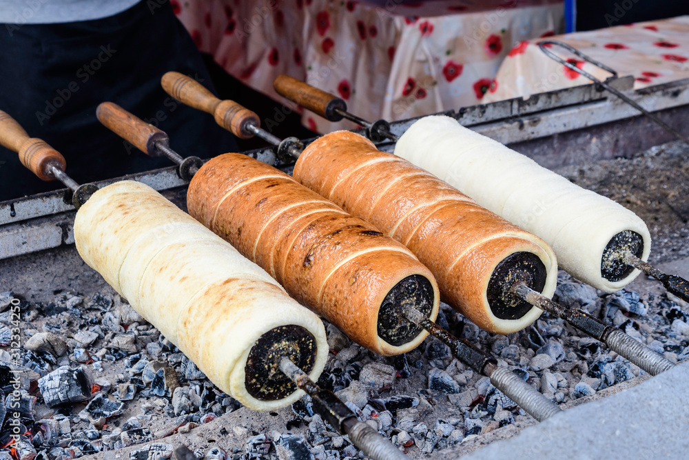 Four fresh Kurtos kalacs (Chimney Cakes) being cooked and glazed with sugar  on rolls spinning and displayed for sale at a local Hungarian market stand,  traditional food photographed with soft focus Stock-Foto