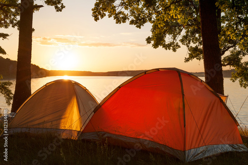 Bright tents on primitive campsite by the picturesque lake at sunset