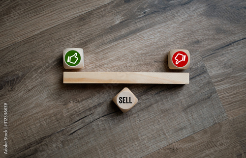 Cubes and dice showing the word sell with thumbs up and down on wooden background