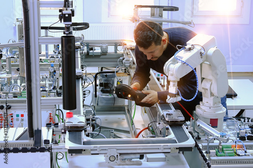 industry 4.0 concept: close-up of an engineer who is teaching robot arm the points with control panel (teach pendant) on smart factory production line. Selective Focus.
