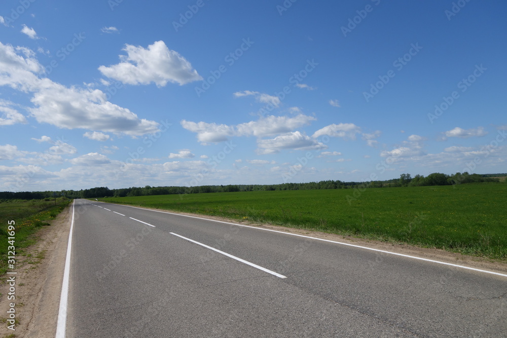 open empty road blue sky with dispersed clouds and green fields