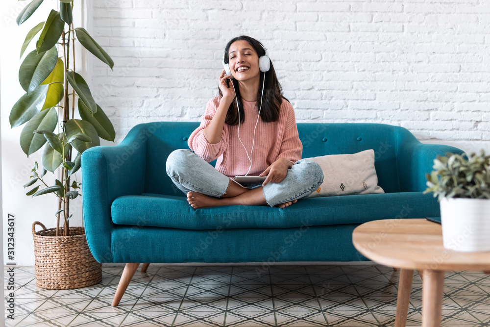 Obraz premium Pretty young woman listening to music with digital tablet and relaxing while sitting on sofa at home.