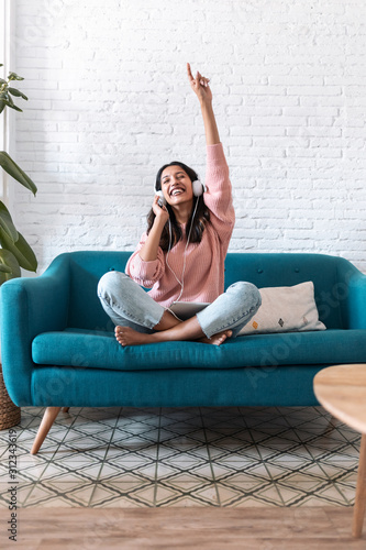 Fotografie Motivated young woman listening to music with digital tablet while sitting on sofa at home