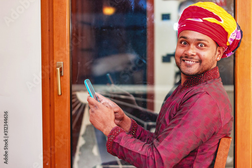 smiling indian man wearing traditional shalwar kameez using smart phone photo