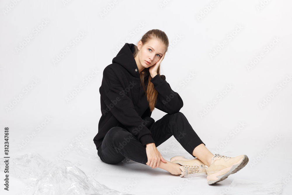 Young girl wearing blank and oversize black long hoody and balck jeans pants . Sitting on white background. Isolated. Young girl wearing blank and oversize black long hoody and balck jeans pants . Sitting on white background. Isolated.