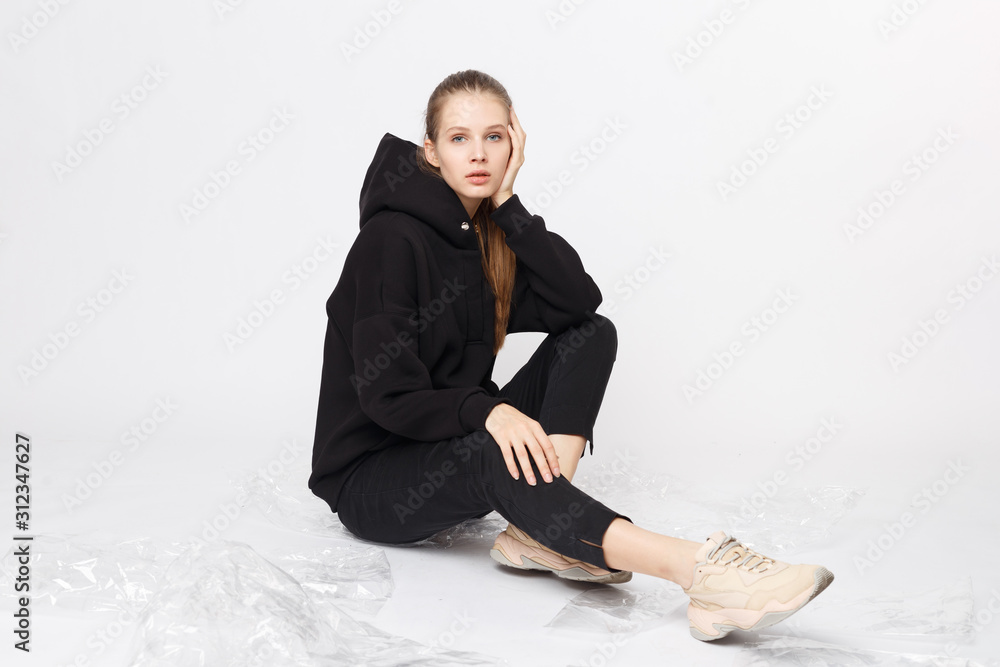 Young girl wearing blank and oversize black long hoody and balck jeans pants . Sitting on white background. Isolated. Young girl wearing blank and oversize black long hoody and balck jeans pants . Sitting on white background. Isolated.