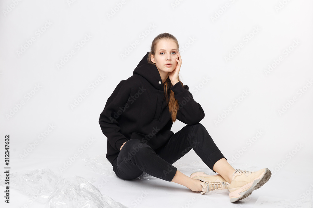 Young girl wearing blank and oversize black long hoody and balck jeans pants . Sitting on white background. Isolated. Young girl wearing blank and oversize black long hoody and balck jeans pants . Sitting on white background. Isolated.