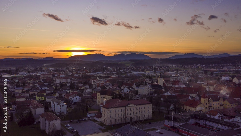 Aerial hyper-lapse of sunsest above a small historic town in Europe, tranquil cityscape in twilight, sundown behind mountains in far background