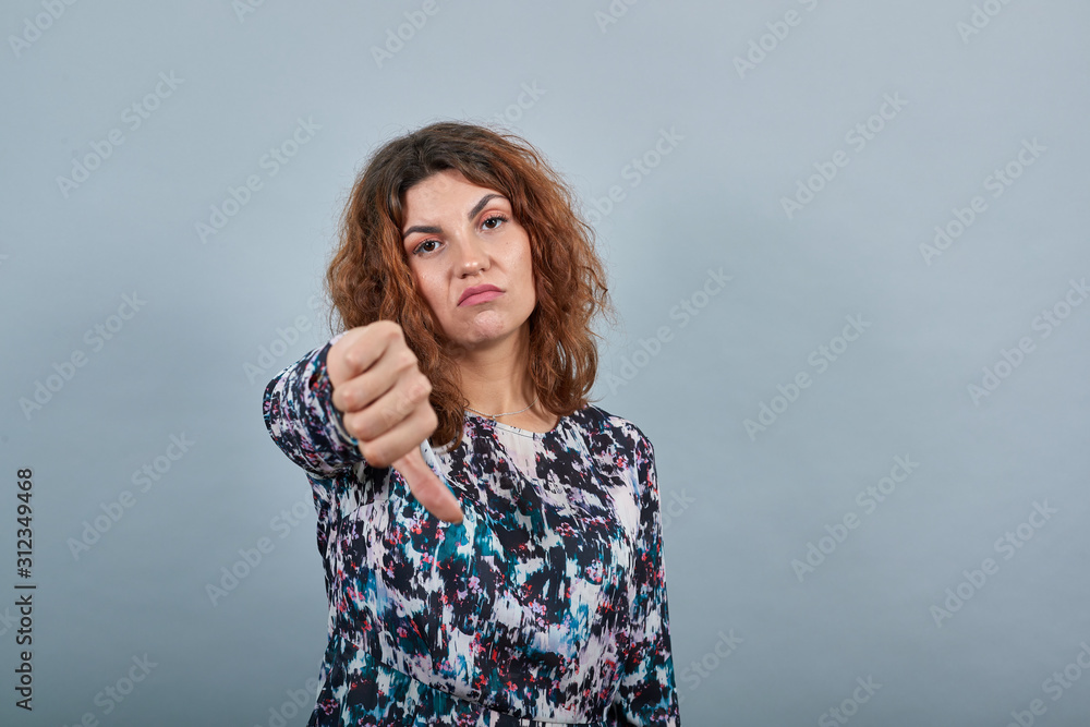 Pretty caucasian young woman keeping thumb down, looking disappointed over isolated gray background in fashion shirt. Lifestyle concept Pretty caucasian young woman keeping thumb down, looking disappointed over isolated gray background in fashion shirt. Lifestyle concept