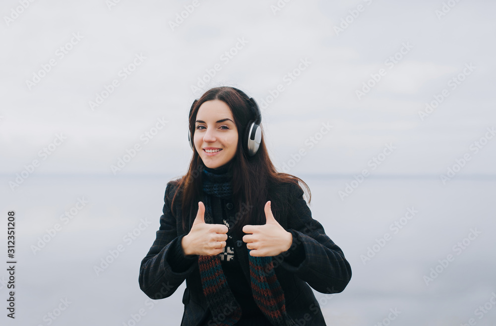 Two hands show thumb up in the form of like. Young caucasian girl in the headphones listens to her favorite music and smiles with pleasure. Mood. Radio concept. Copy space. Two hands show thumb up in the form of like. Young caucasian girl in the headphones listens to her favorite music and smiles with pleasure. Mood. Radio concept. Copy space.