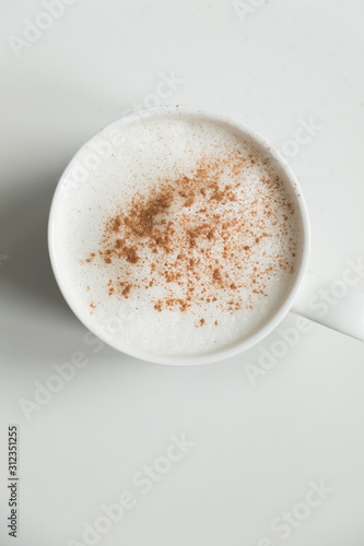 Mug in which cappuccino coffee with froth sprinkled with grated cinnamon. Shot from above on a white background