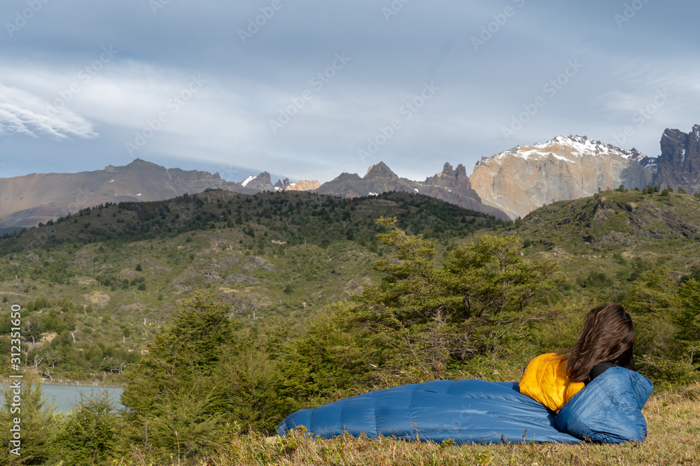 Girl in sleeping bag in mountains near lake