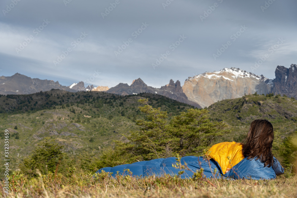 Girl in sleeping bag in mountains near lake