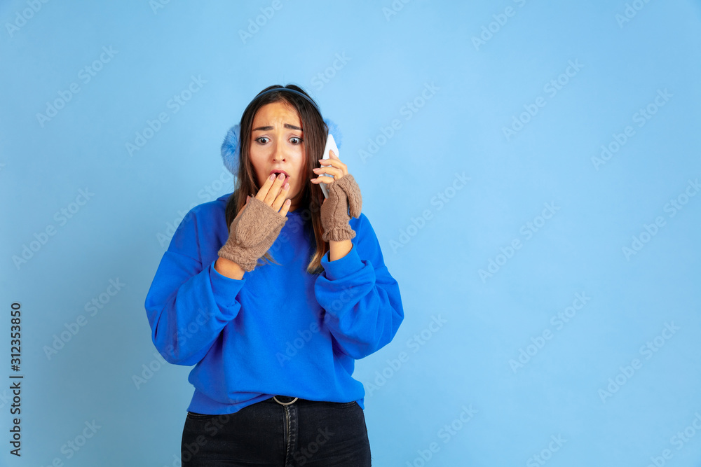 Talking on phone. Caucasian woman's portrait on blue studio background. Beautiful female model in warm clothes. Concept of human emotions, facial expression, sales, ad. Winter mood, Christmas time Talking on phone. Caucasian woman's portrait on blue studio background. Beautiful female model in warm clothes. Concept of human emotions, facial expression, sales, ad. Winter mood, Christmas time