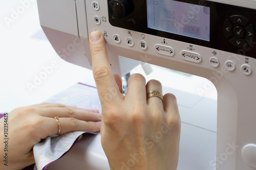 Women's hands sew clothes on a sewing machine. Close-up photo, white background.