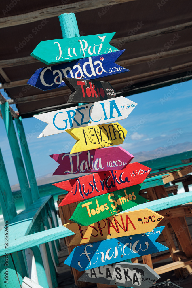 Fototapeta premium Colorful wooden direction signpost with destination countries at Playa El Tecolote near La Paz, Mexico