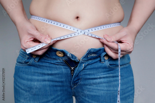 Overweight and obesity concept, fat belly, woman in unbuttoned jeans with measuring tape around the waist. Weight loss, slimming and diet, health care