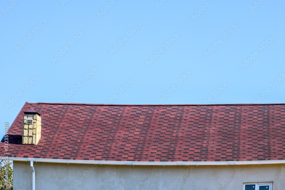 Roof from multi-colored bituminous shingles. Patterned bitumen shingles. Bituminous burgundy roof.