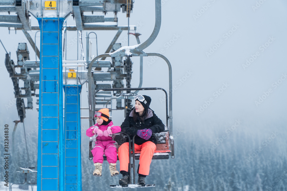 Fototapeta premium Happy family enjoying winter vacations in mountains . Mother with her daughter on the ski lift.
