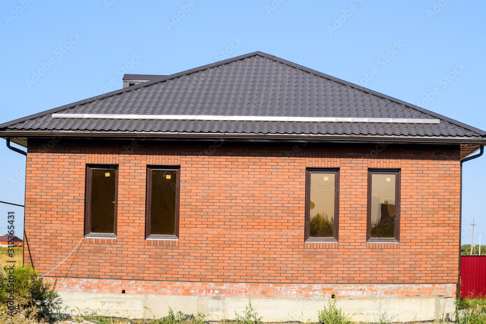 The house with plastic windows and a roof of corrugated sheet. Brown roof and brown brick