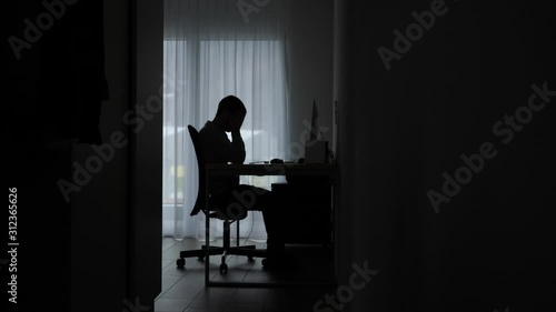 Silhouetted man in room by computer stressed, overwhelmed and fatigued. photo