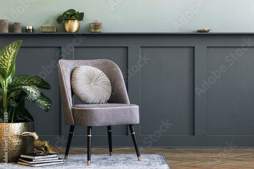 Modern composition of living room with design gray armchair, gold pot with beautiful plant, books and elegant personal accessories. Gray wall panelling with shelf. Stylish home staging. Template. 