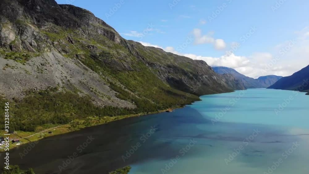 Aerial, tracking, drone shot, overlooking the Gjendesheim turisthytte and turquoise water, of lake Gjende, birds in frame, on a sunny, summer day, in Jotunheimen National park, Lom, Oppland, Norway Aerial, tracking, drone shot, overlooking the Gjendesheim turisthytte and turquoise water, of lake Gjende, birds in frame, on a sunny, summer day, in Jotunheimen National park, Lom, Oppland, Norway