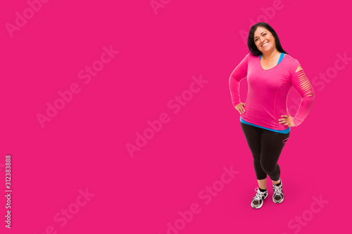 Middle Aged Hispanic Woman In Workout Clothes Against A Bright Pink Background.