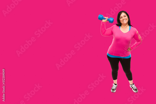 Middle Aged Hispanic Woman In Workout Clothes Holding Dumbbell Against A Bright Magenta Pink Background © Andy Dean