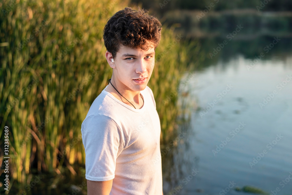 A teenage boy on a background of lakes and reeds, resting after a morning jog. The guy in the ear has a medical cotton wool because he has a sick ear A teenage boy on a background of lakes and reeds, resting after a morning jog. The guy in the ear has a medical cotton wool because he has a sick ear