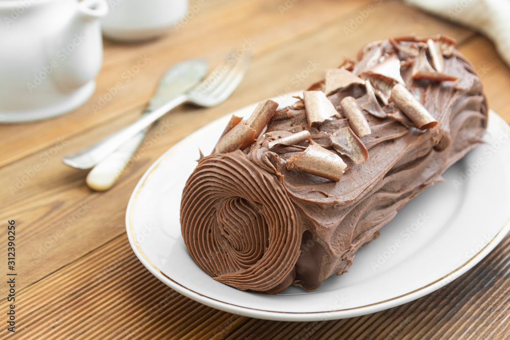 Chocolate swiss roll isolated on a wooden background. Chocolate sweet dessert. Pastry for breakfast or tea.