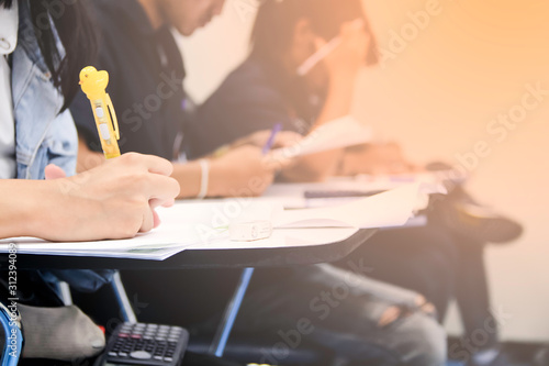 Hands university student holding pen writing /calculator doing examination / study or quiz, test from teacher or in large lecture room, students in uniform attending exam classroom educational school.