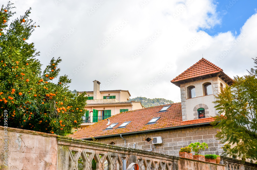 Streets of beautiful city Valldemossa in Mallorca, Spain. Historical buildings and orange tree on a cloudy day. Old town of the Spanish city. Tourist destinations