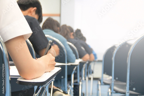 Hands university student holding pen writing /calculator doing examination / study or quiz, test from teacher or in large lecture room, students in uniform attending exam classroom educational school. photo