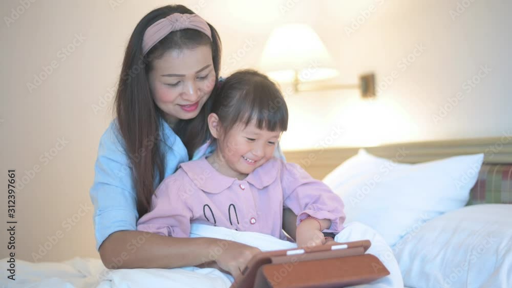 Mother and daughter using tablet with laugh happy feeling on white bed concept for happy family Mother and daughter using tablet with laugh happy feeling on white bed concept for happy family